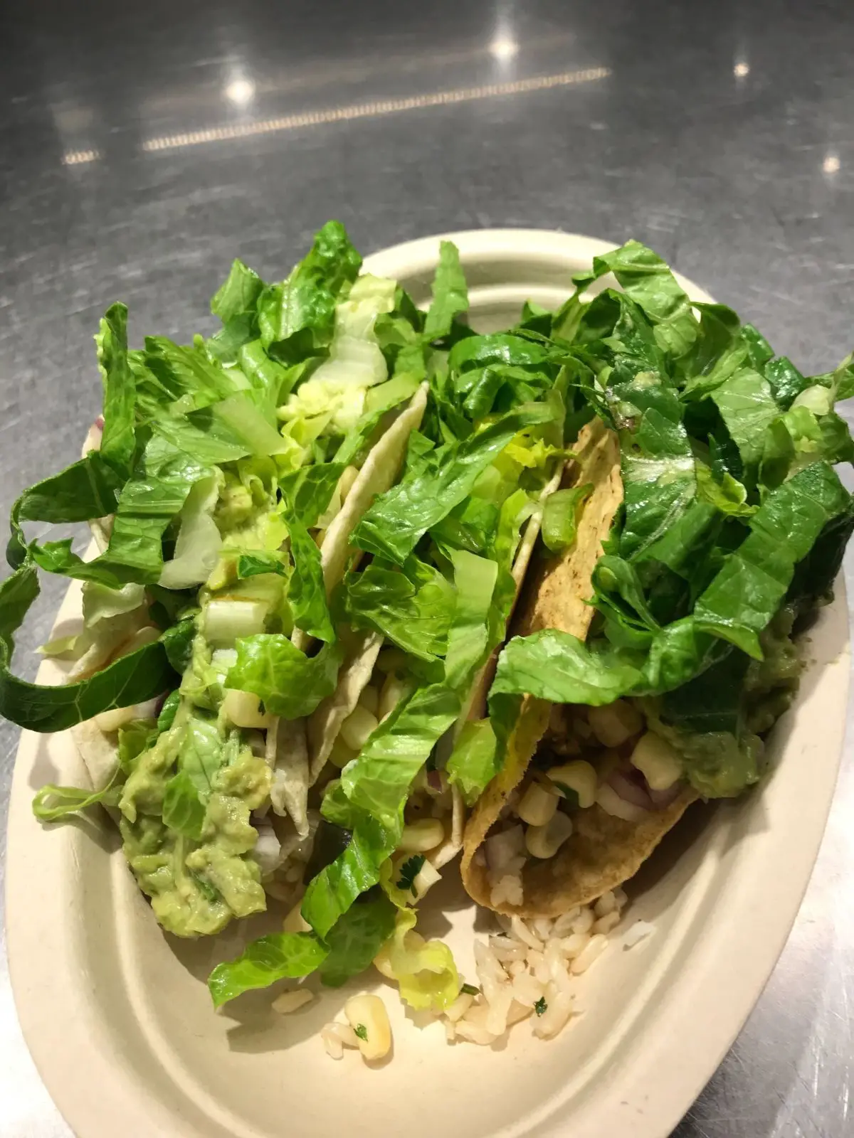 vegan tacos from chipotle in a bowl with lettuce, rice, corn, guacamole, tortillas, and a taco shell