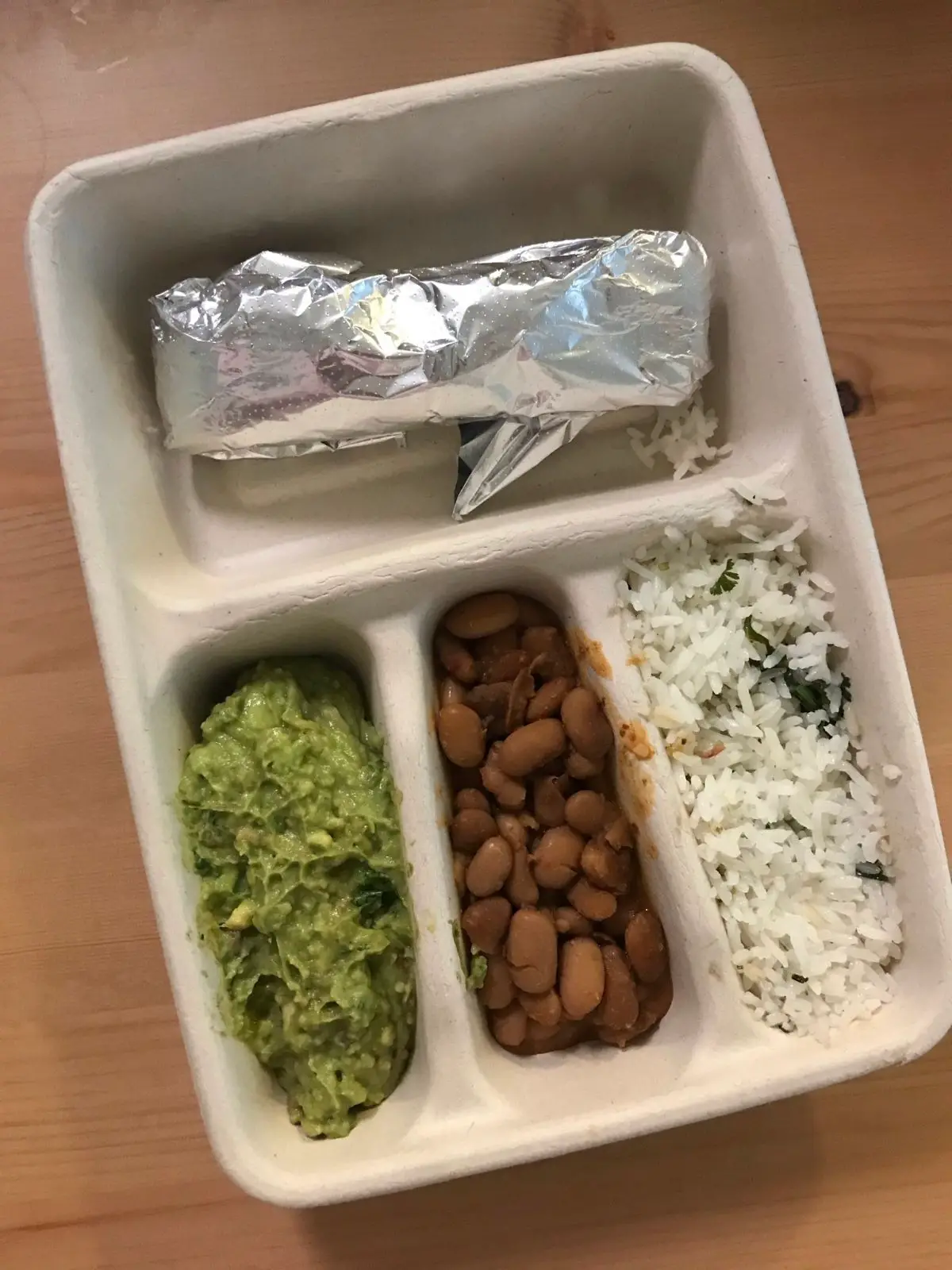 vegan kids meal from chipotle with a tortilla in foil, pinto beans, white rice, and guacamole on a wood table