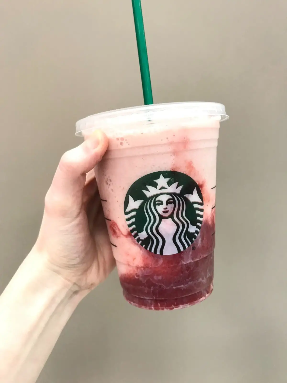 vegan strawberries and cream frappuccino with strawberry syrup on a tan wall