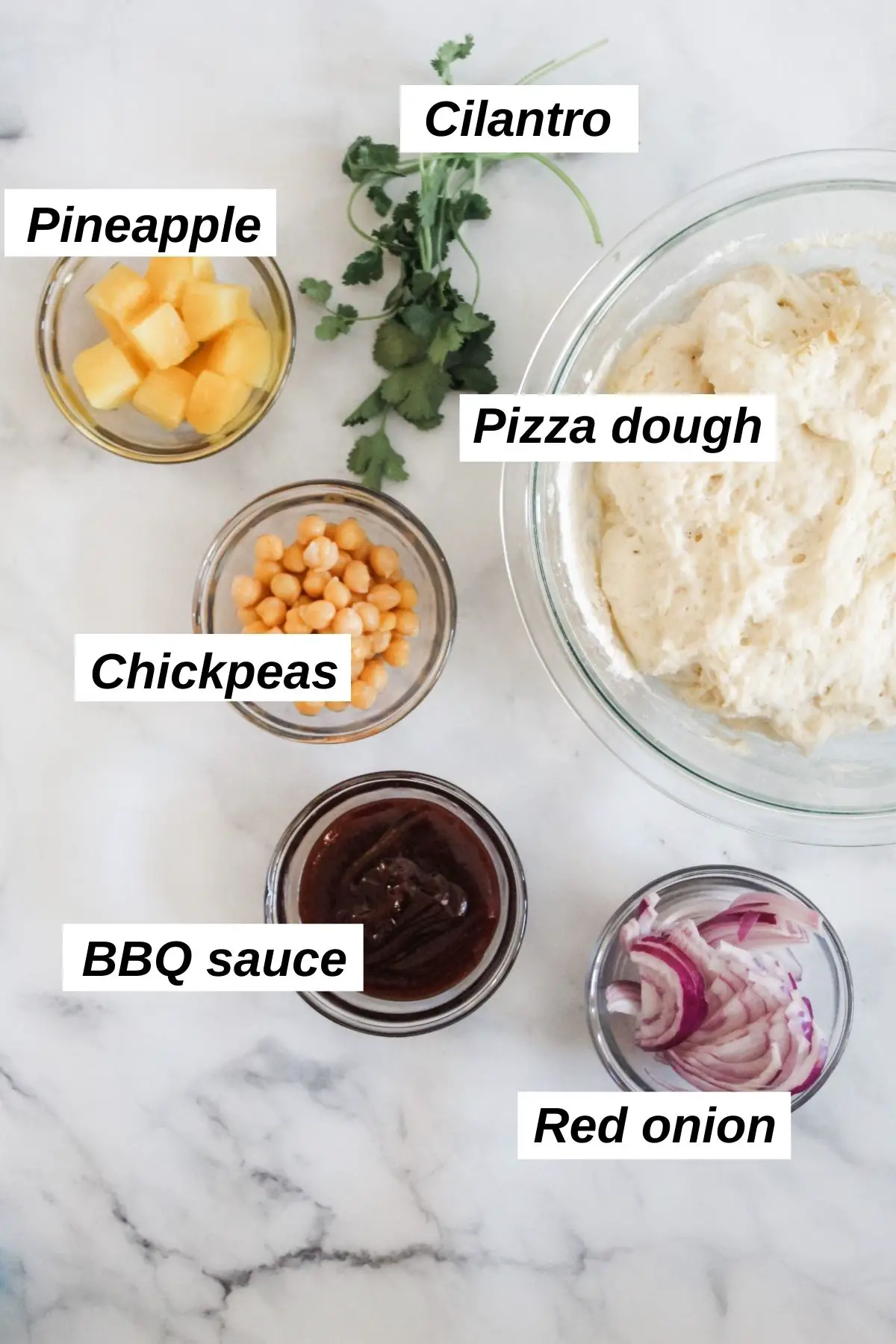 ingredients for vegan bbq pizza in dishes including red onion, pizza dough, cilantro, pineapple, bbq sauce, and chickpeas