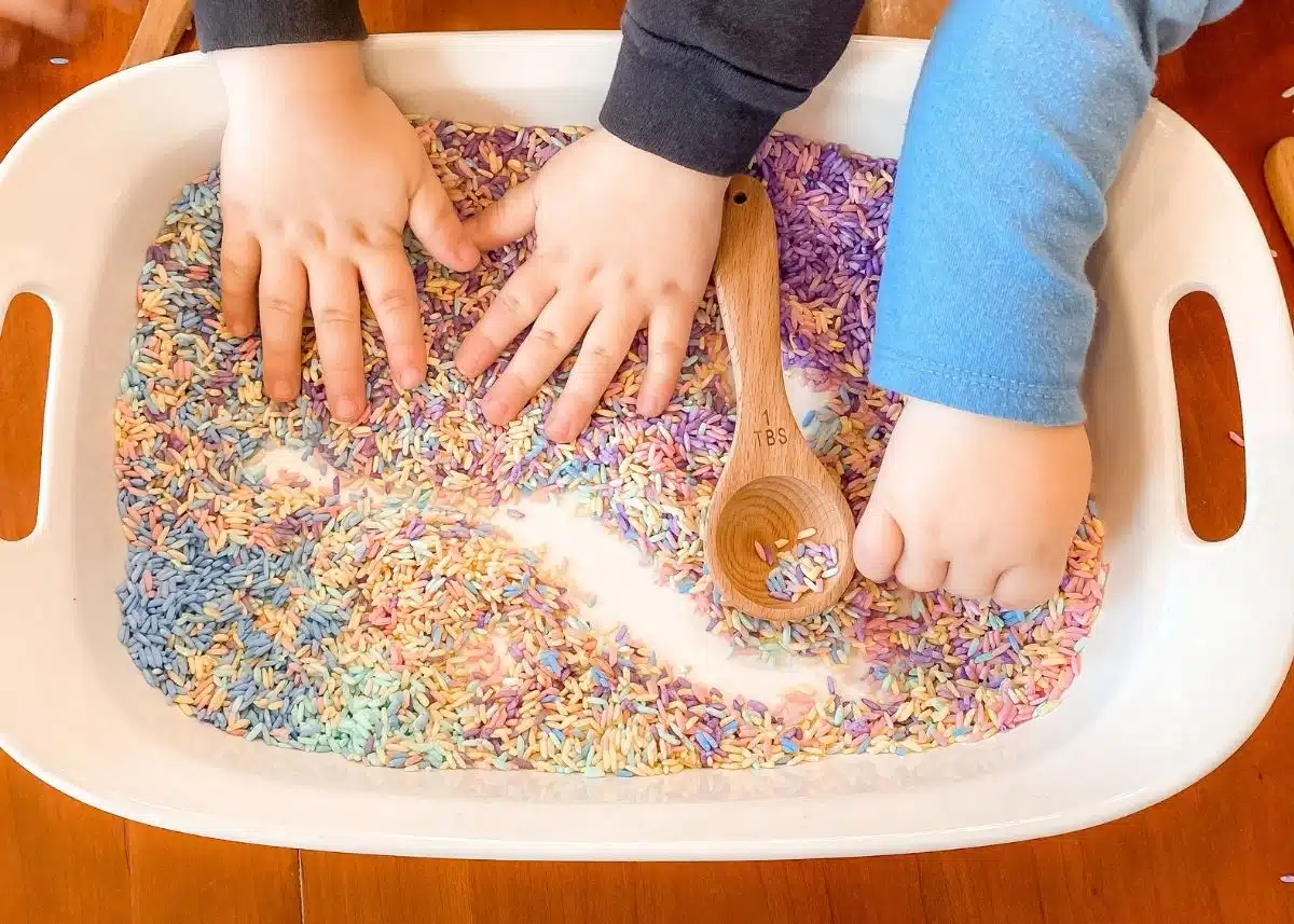 The little hands playing with rainbow rice.  One sensory play benefit is it helps their fine motor skills.