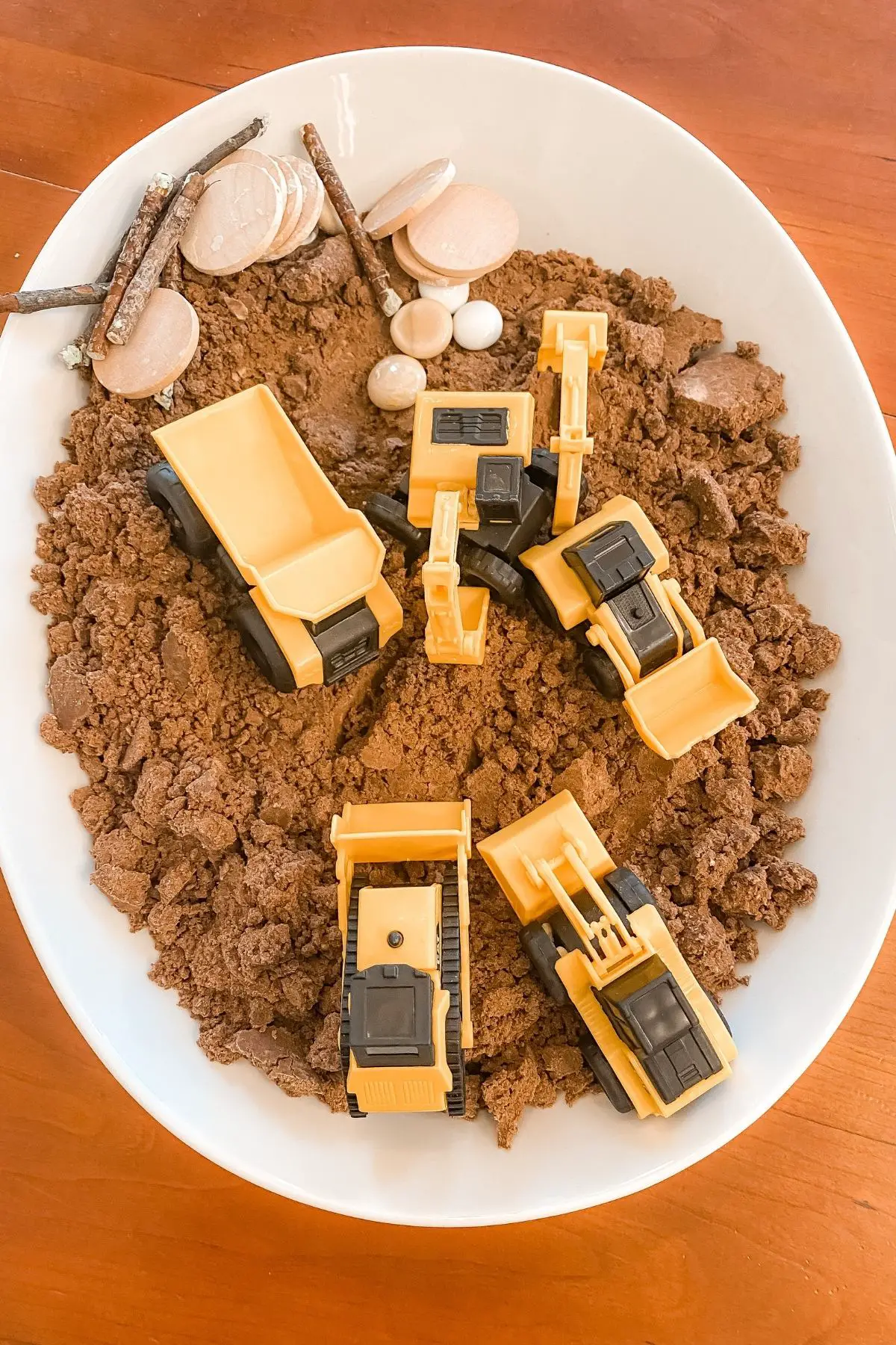 A tray of edible dirt for sensory play with mini construction vehicles, rocks, and sticks.
