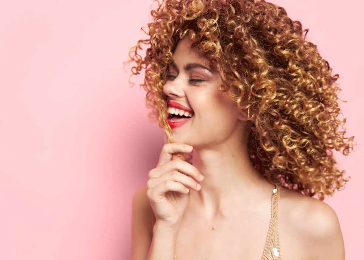 A woman with curly hair is wearing a laughing because she heard funny puns.