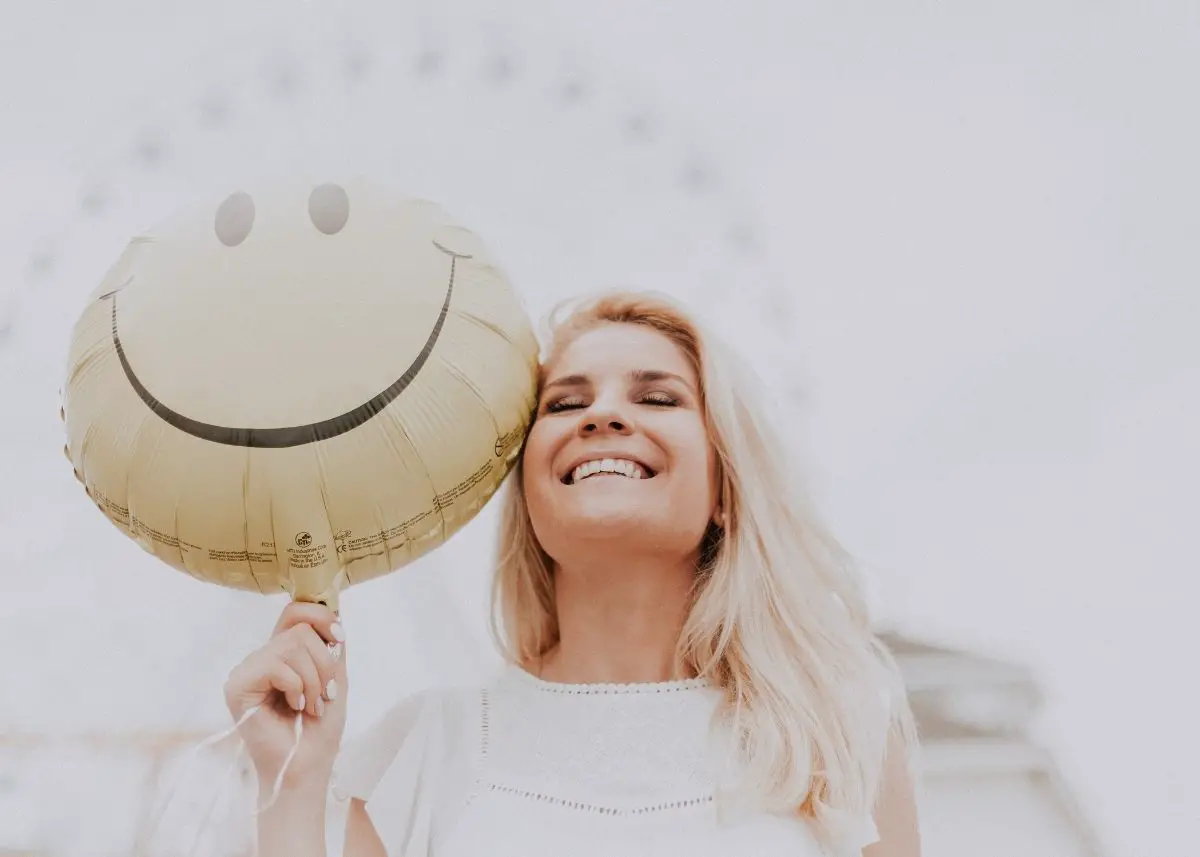 A woman is smiling because she heard a clever pun and she's holding a smiley face balloon.
