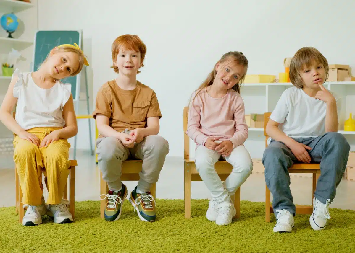 Four kids are sitting on chairs looking at the camera.