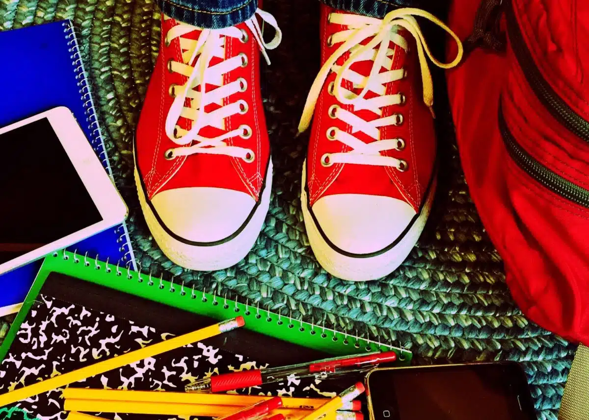 A close up picture of school supplies surrounding a student wearing red converse shoes.
