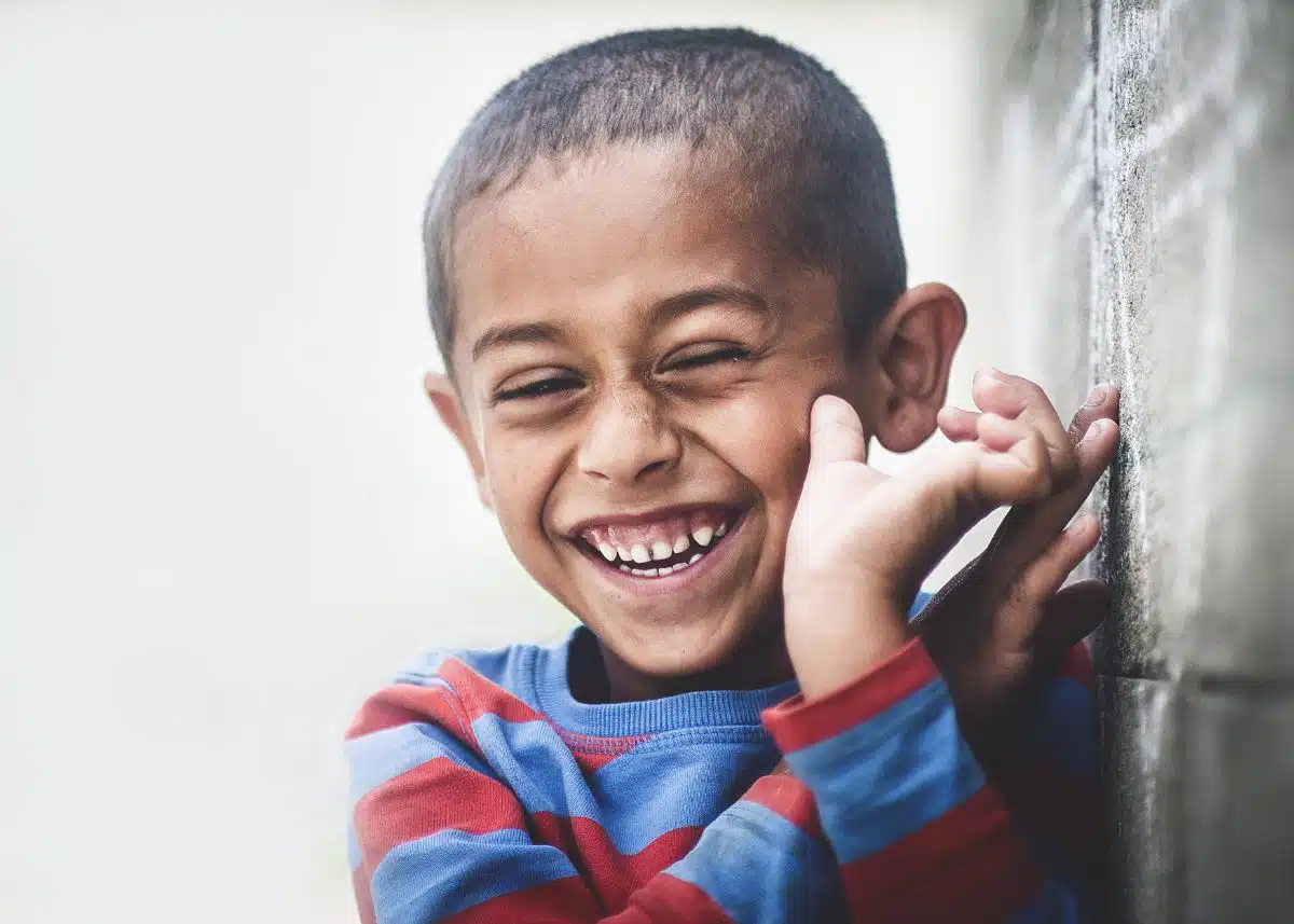 A little boy wearing a blue and red striped sweater is laughing.
