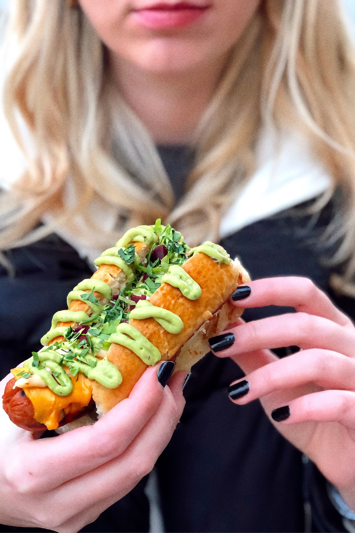 A blond girl is eating a specialty hot dog.