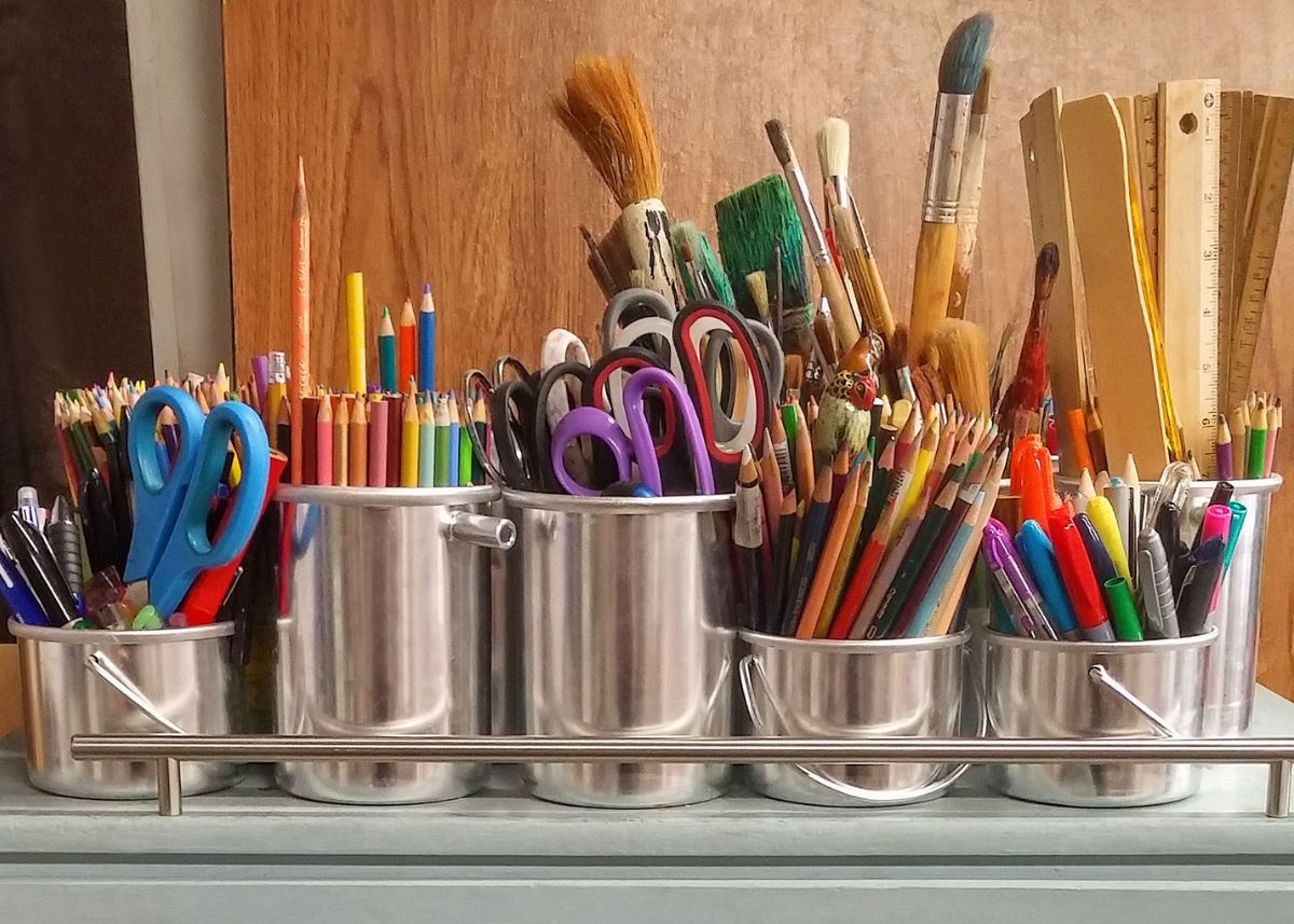 A bunch of art supplies on metal cans.  There are colored pencils, scissors, rulers, and paintbrushes.  