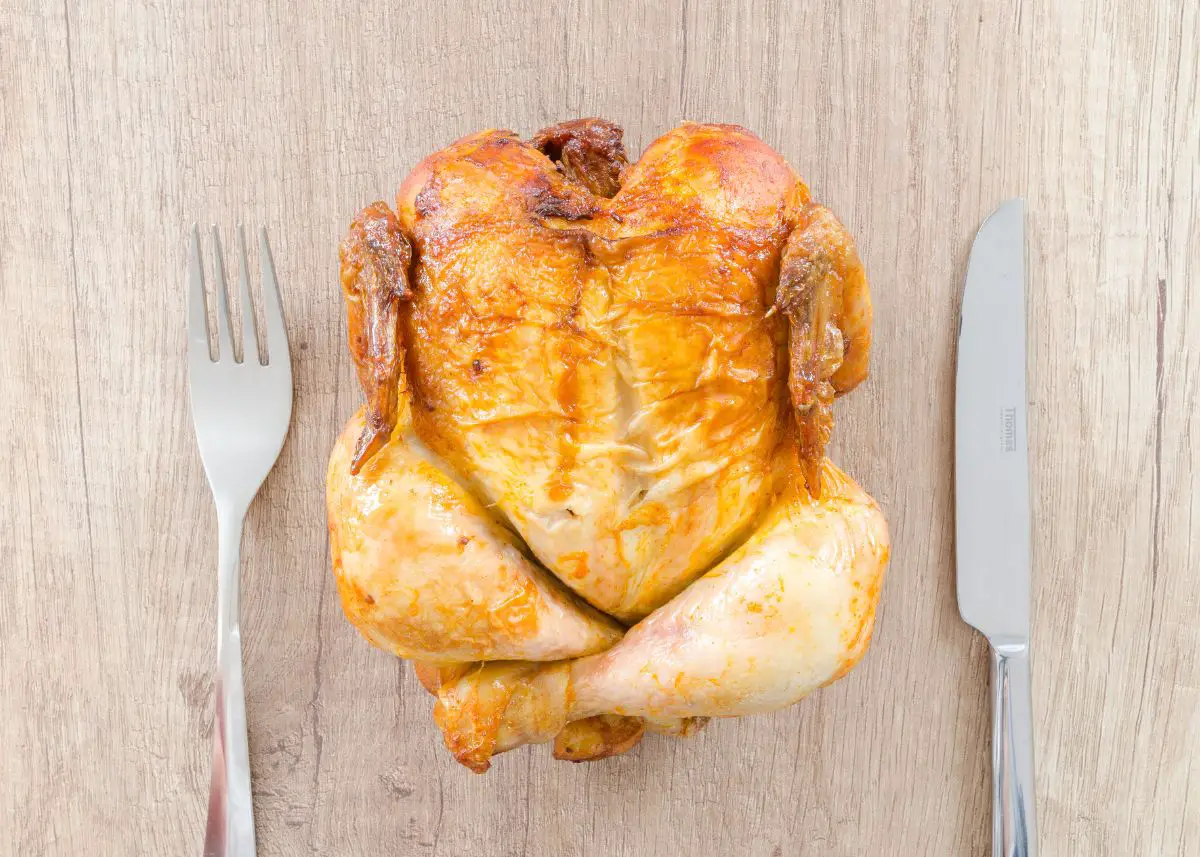 A whole chicken is on a table between a fork and a knife.
