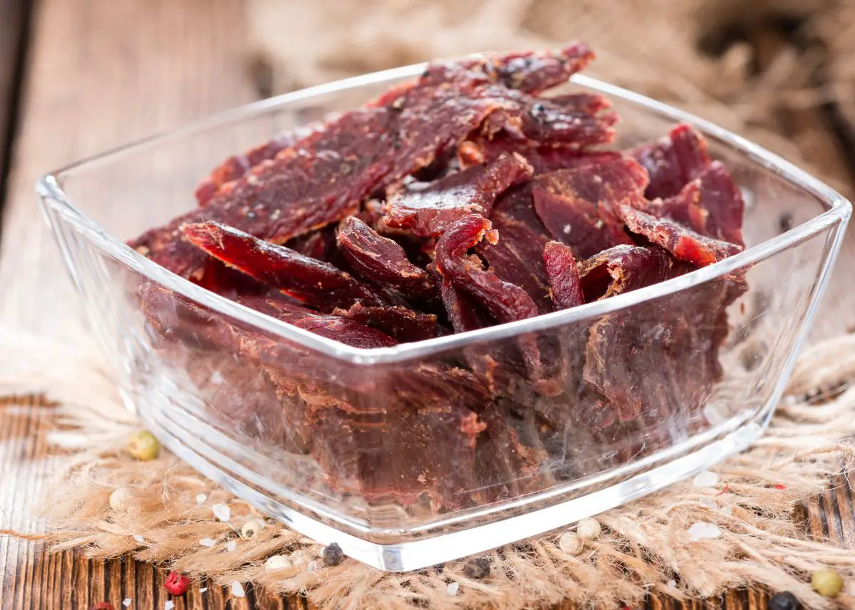 Beef jerky in an airtight container on a wood table.