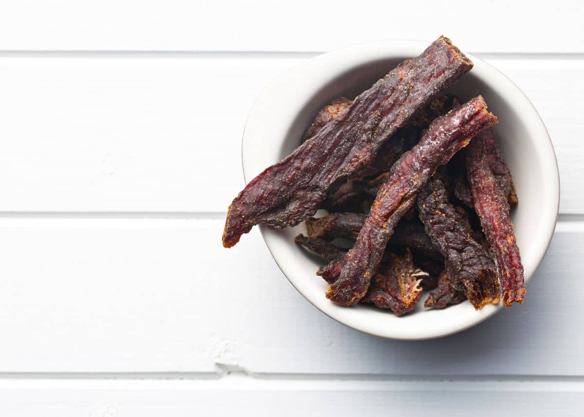 Dark beef jerky in a white bowl with a white background.