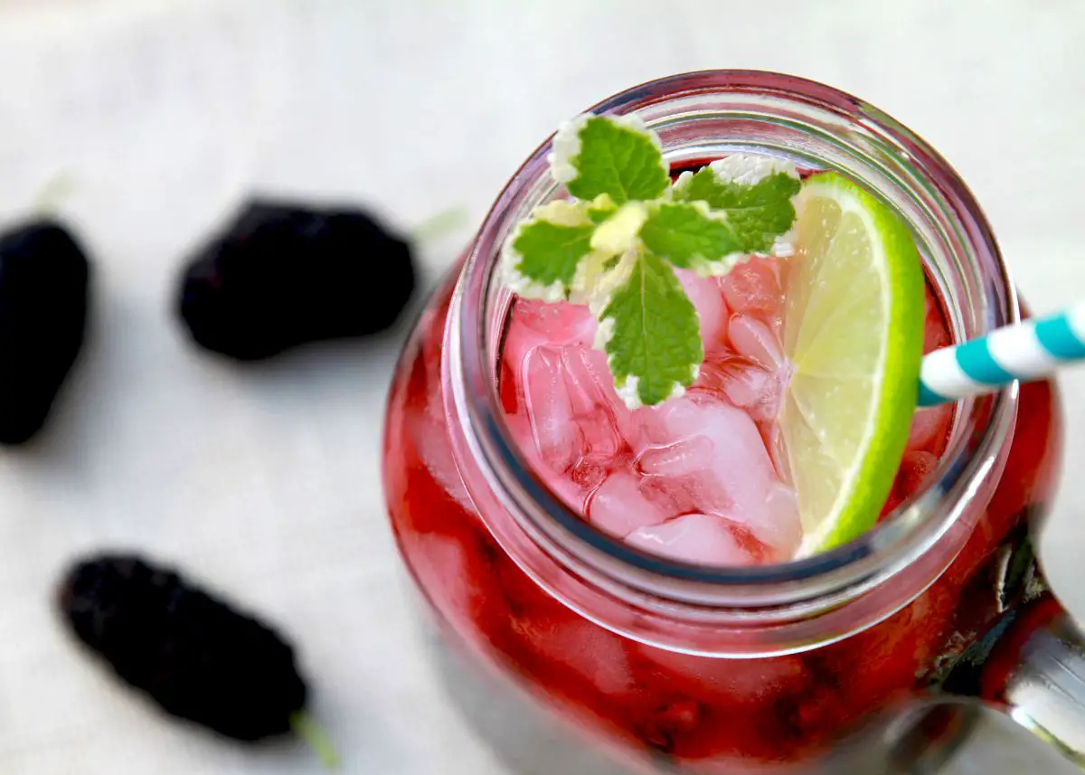 A closeup of blackberry juice in a mason jar with a lime and a blue striped straw.  