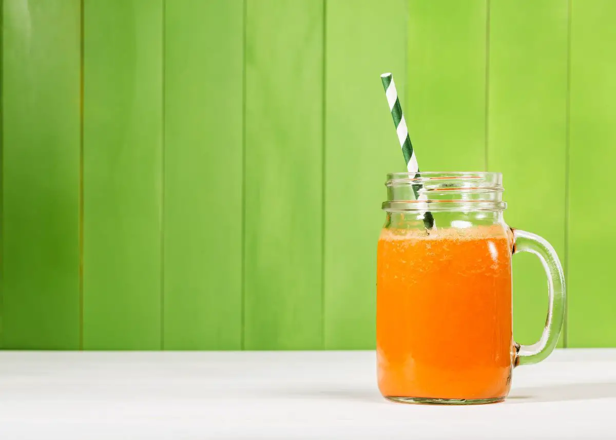 Carrot juice in a mason jar with a green striped straw with a green background.