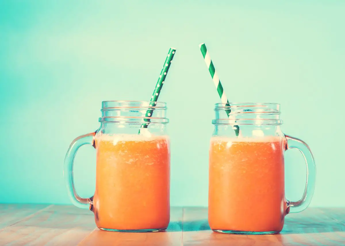 Orange juice in mason jars with green straws with a blue background.  