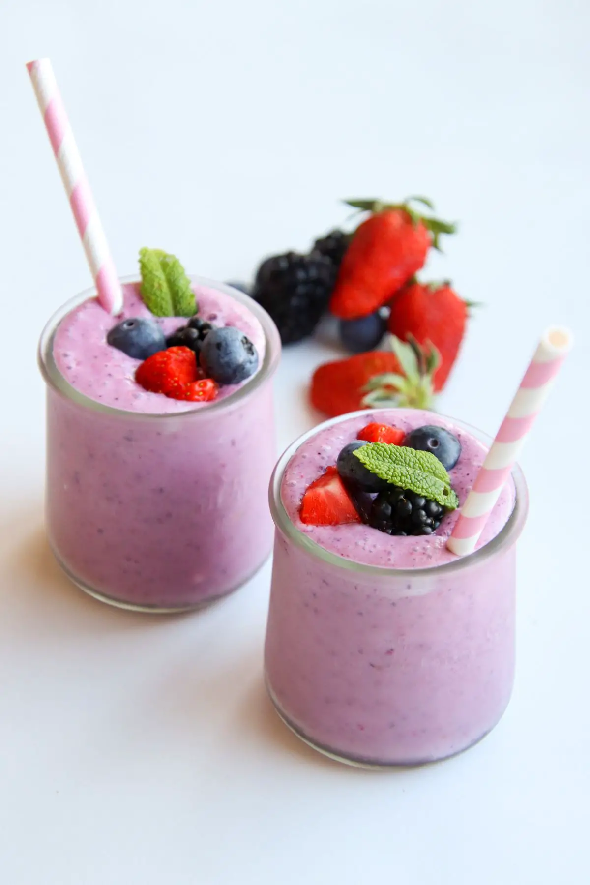 Two berry smoothies with pink striped straws and berries surrounding them.