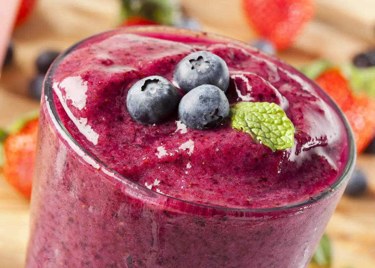 A closeup of a berry smoothie with three blueberries on the top.  It's surrounded by berries.