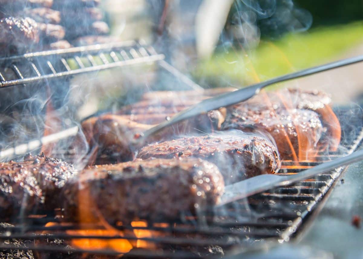 Five hamburger patties and six hot dogs are being cooked on a grill. 