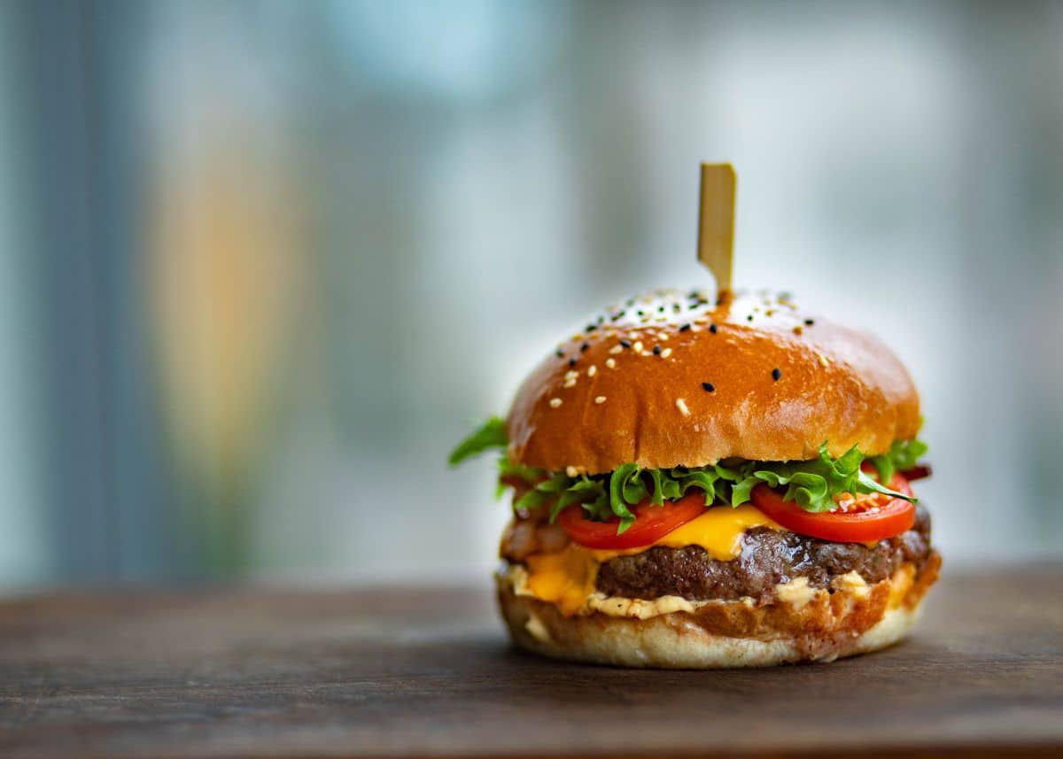 A closeup of a cheeseburger with tomatoes and lettuce on a sesame bun.  