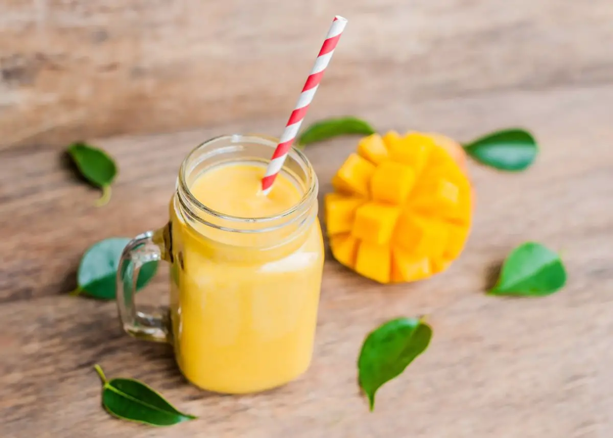 A mango smoothie with a red striped straw with a cut mango and mint leaves around it.