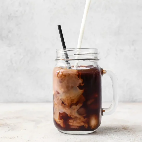 Cream being poured into an iced coffee in a mason jar
