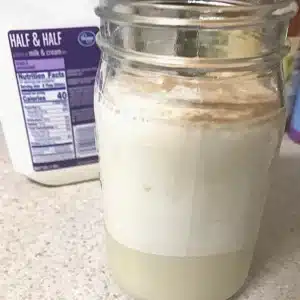 A side shot of all the ingredients together in a mason jar, with a container of half and half in the background