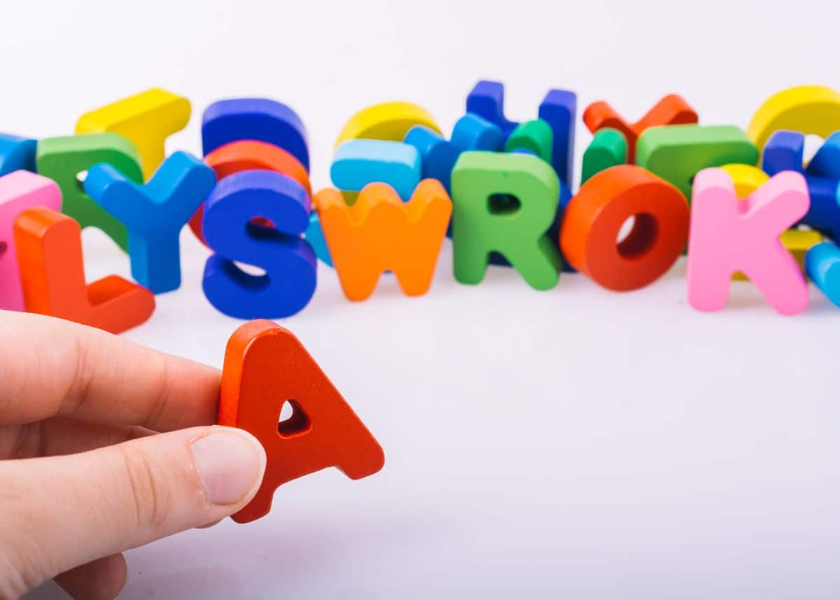 Someone is holding a plastic letter A in front of the rest of the letters of the alphabet.  They look like the letter magnets kids can playwith on the fridge.