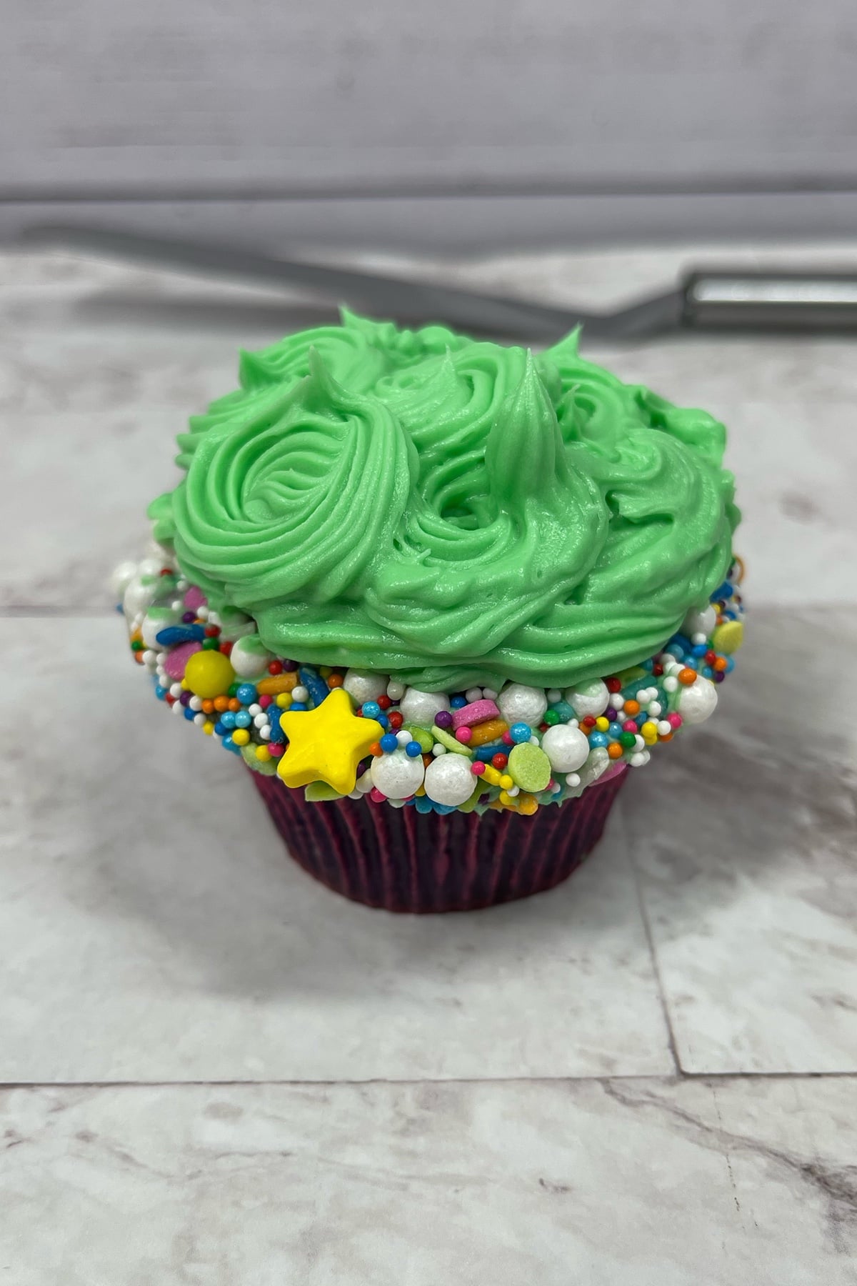 Cupcake with green frosting and rainbow sprinkles marbled background