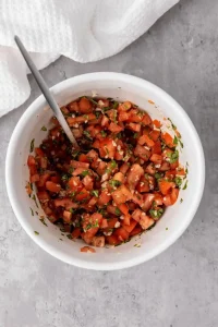 Mixed together Bruschetta in large bowl sitting on a marble countertop with a white kitchen towel nearby