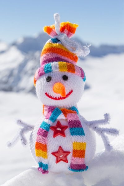 This is a closeup of a knit snowman.  It has a pink, purple, blue, orange, yellow, and white scarf and hat.  