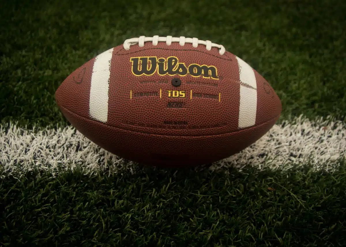 This is a closeup of a football on a yard line.  You can see the threads and the "Wilson" brand.