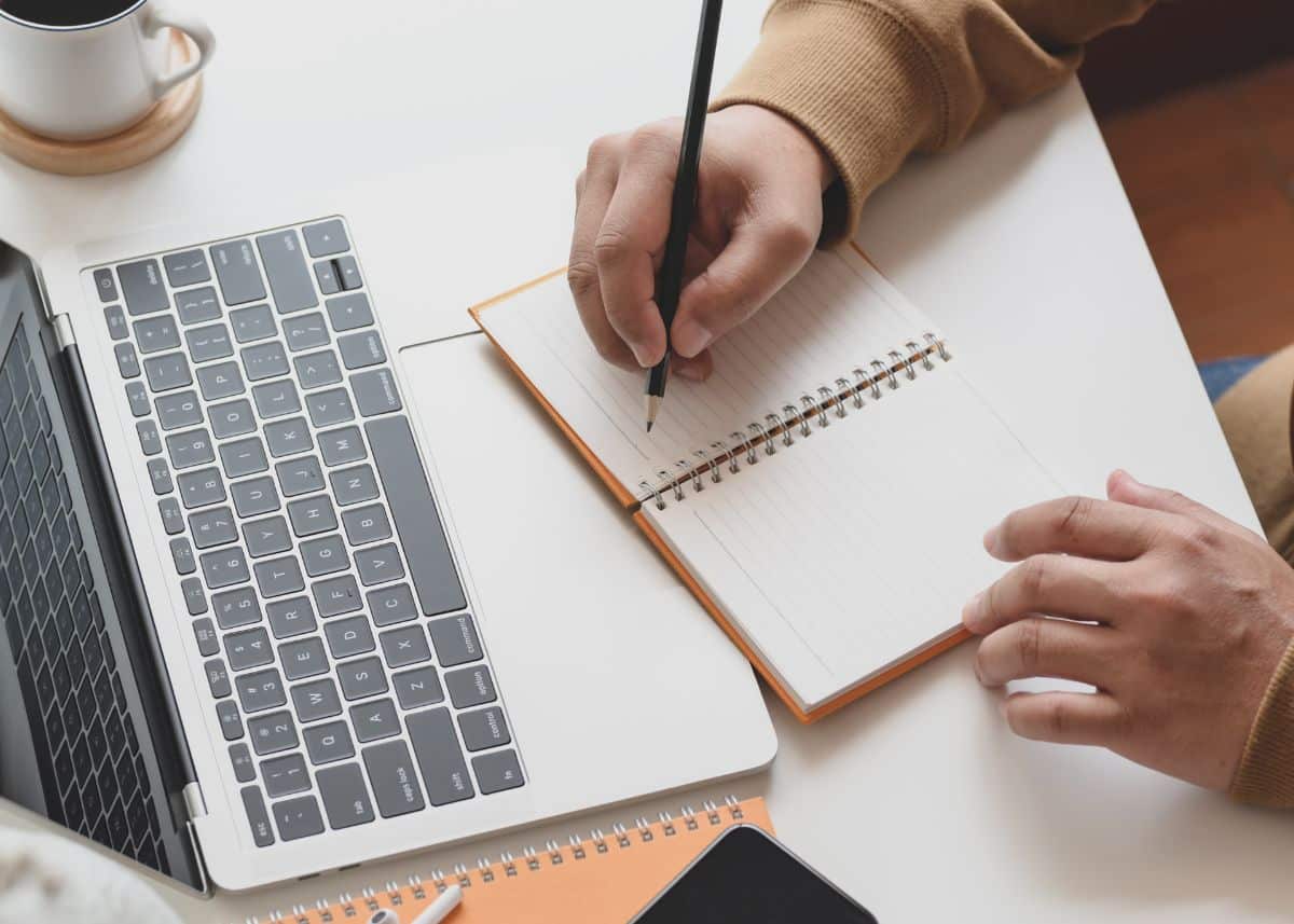 This is a bird's eye view of someone working at a desk.  There is a laptop and they're writing in a notebook.