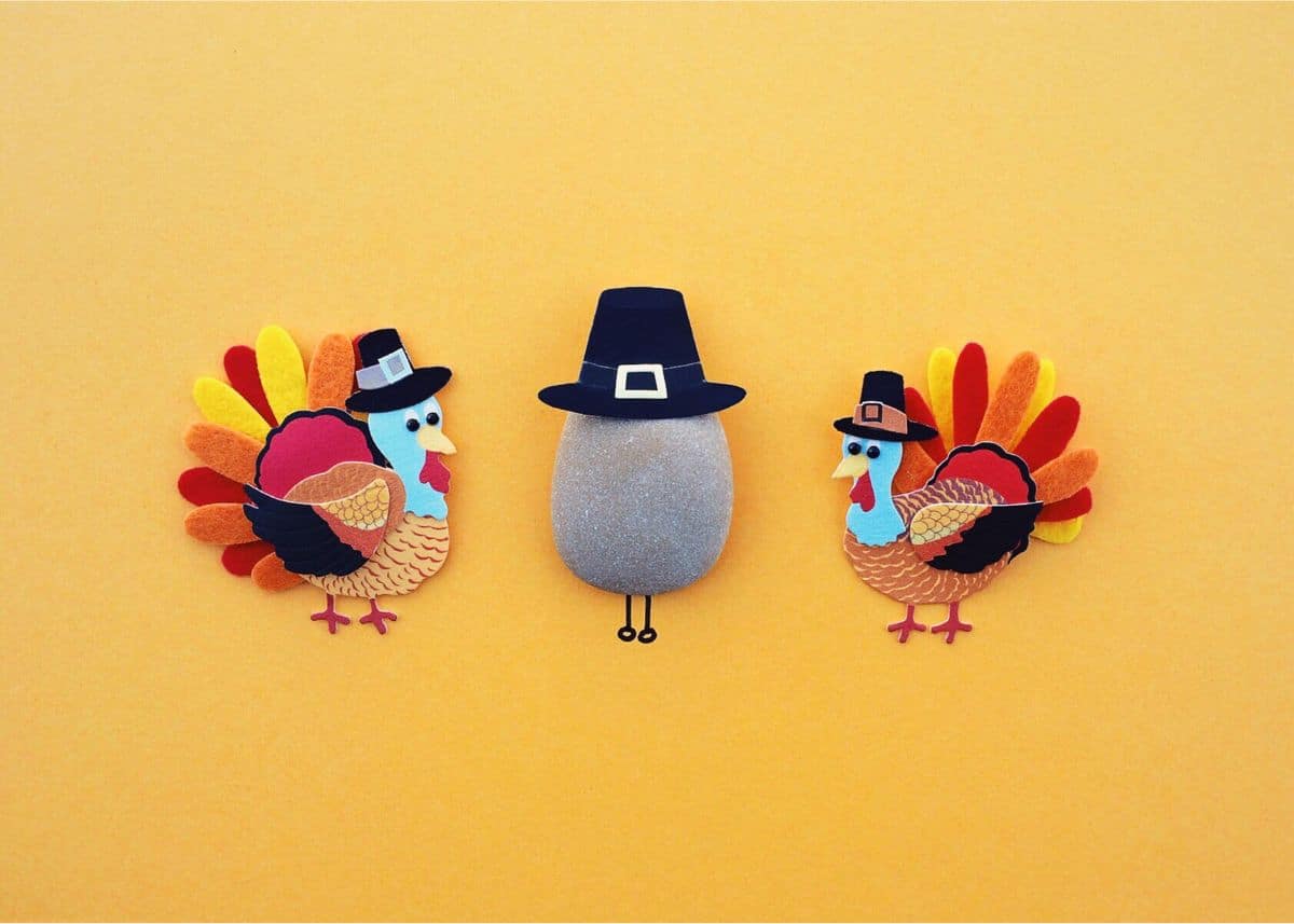 This is a photo of two felt turkeys wearing Pilgrim hats.  There is a rock in the middle with a Pilgrim hat.