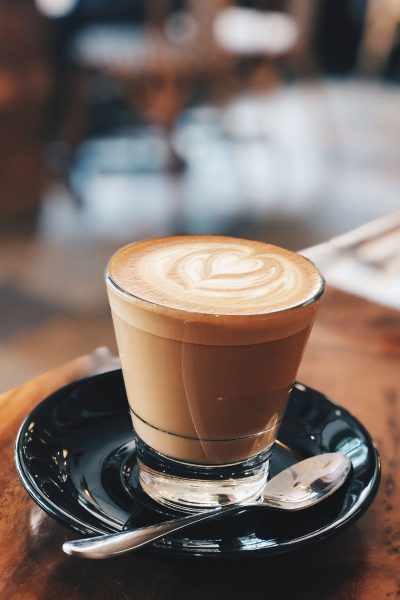 Glass of coffee with a cream swirl on a black plate with a spoon.