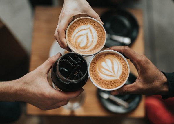 Three people holding cups of coffee together.