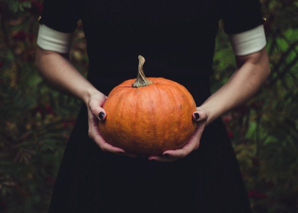 A woman wearing a black dress is holding a pumpkin.