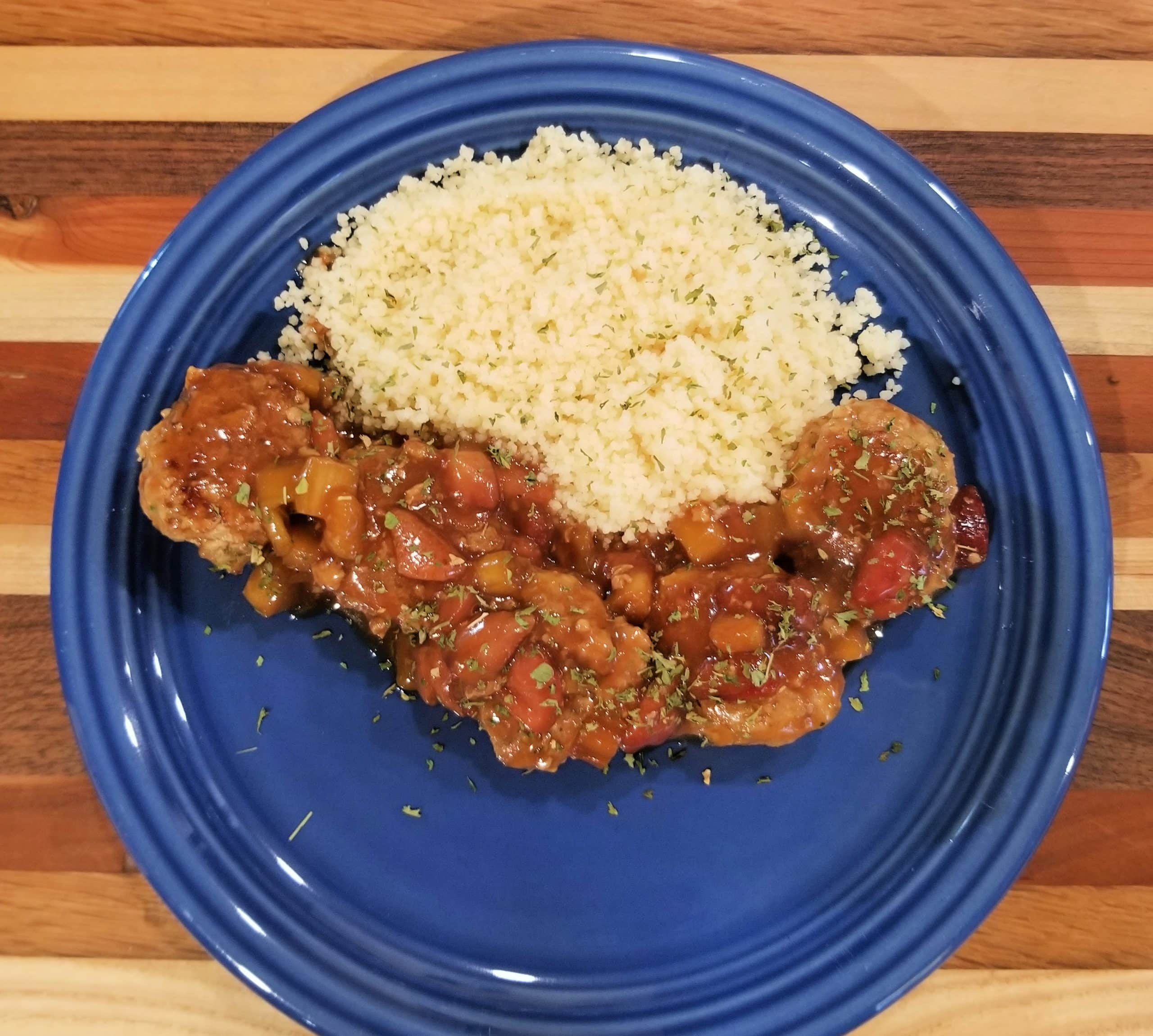 5 meatballs topped by strawberry rhubarb sauce on a blue plate with a serving of couscous
